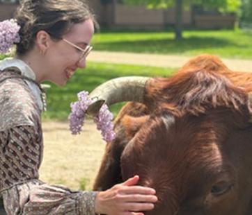 Woman in period clothes petting cow on a sunny spring day